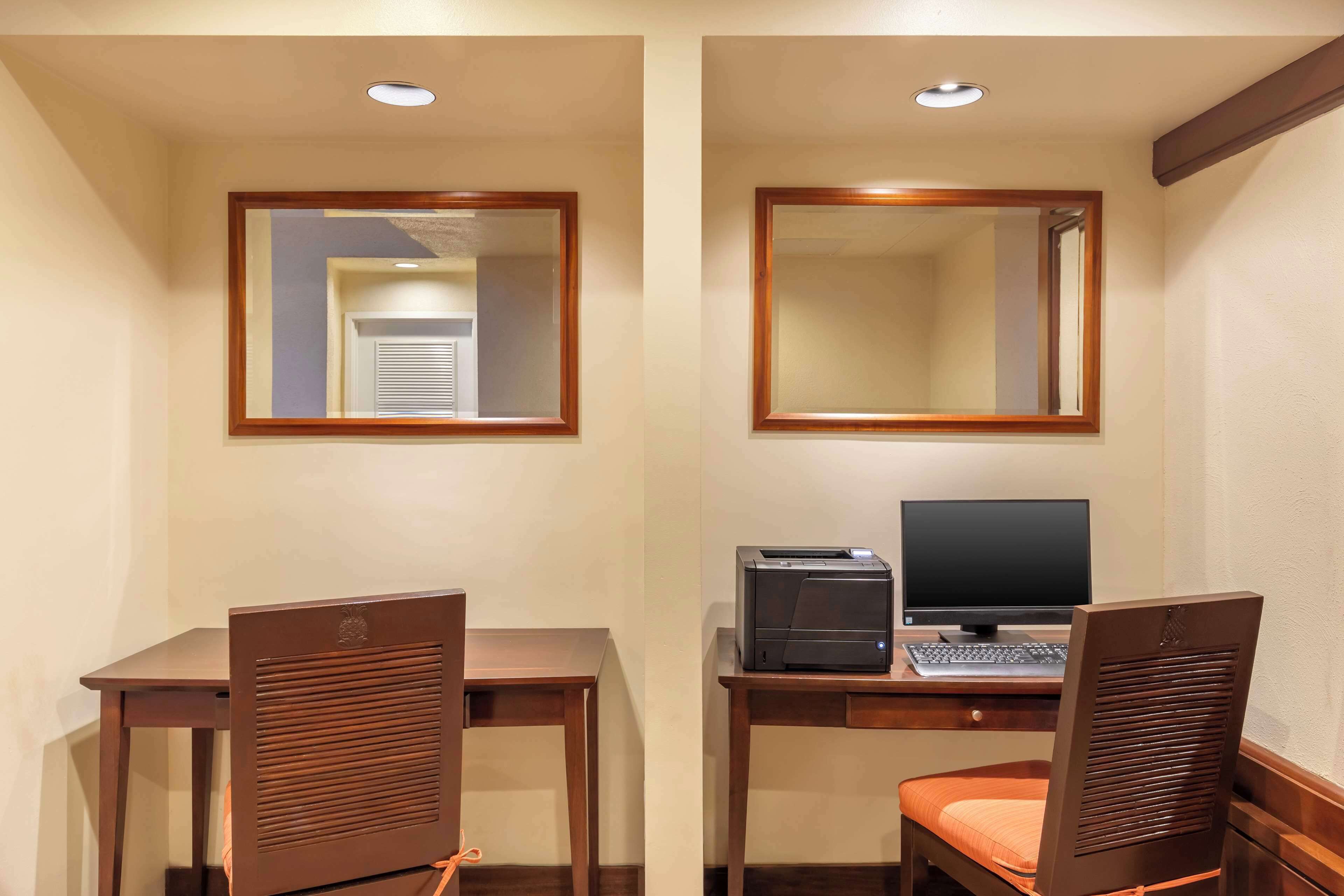 A hotel room with two wooden desks, each with a chair, a computer, and a printer. There are two mirrors above the desks.