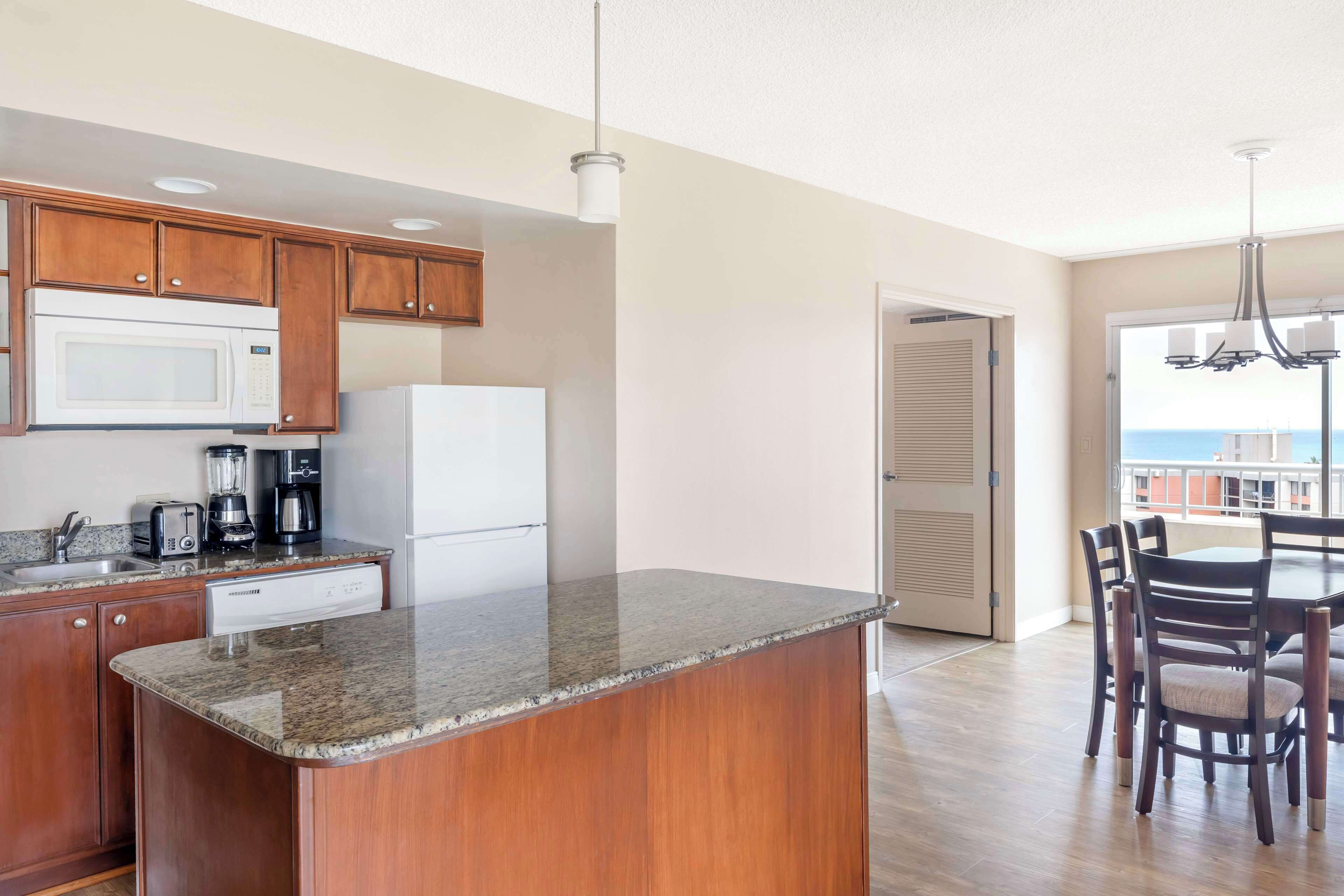 A kitchen with wooden cabinets, a granite countertop, a microwave, a coffee maker, and a refrigerator.