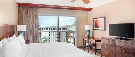 A hotel room with a large bed, a desk with a chair, a television, and a balcony with a view of the city.