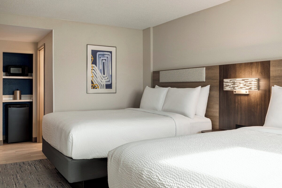 A hotel room with two beds, a microwave, a mini-fridge, and a trash bin.