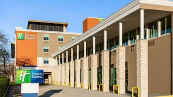 A Holiday Inn Express hotel with a modern design, featuring a central atrium with columns, a parking lot, and a clear sky.