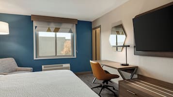 Habitación de hotel con cama, escritorio, silla, televisor y ventana con cortinas.