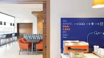 Un espace repas moderne doté d’un bar pour le petit-déjeuner, de sièges et d’un appareil à café mural.