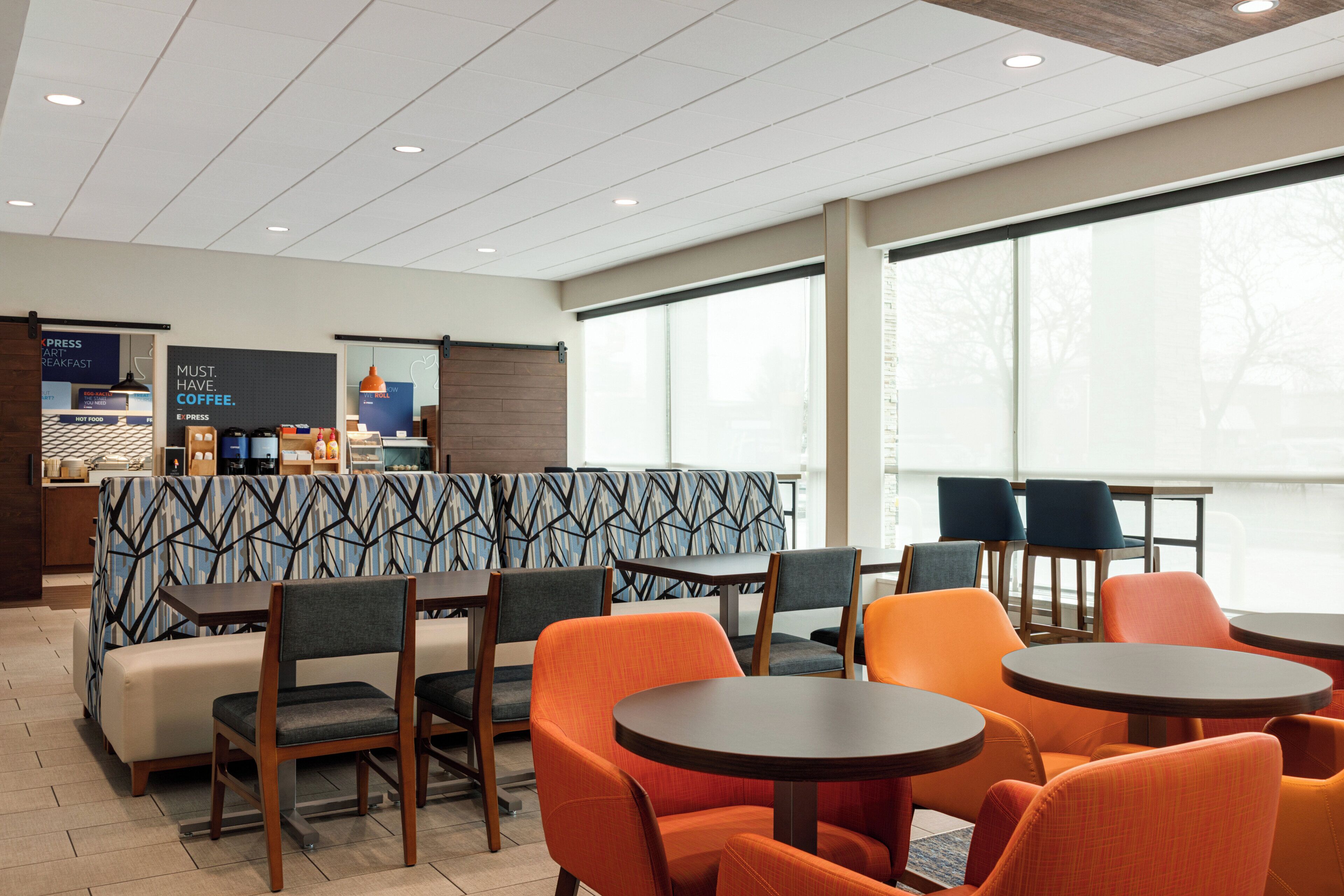 A modern cafe with seating arrangements, a coffee station, and large windows providing natural light.
