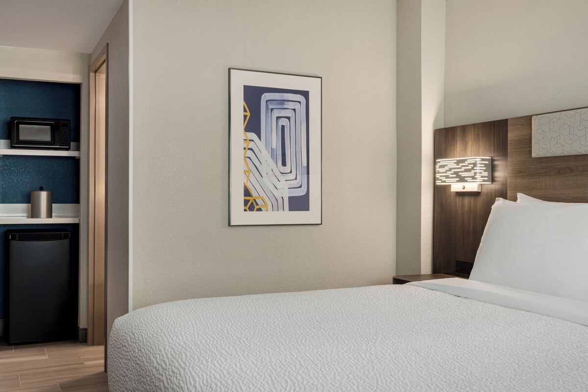 A hotel room with a bed, a microwave, a refrigerator, and a wall-mounted artwork.