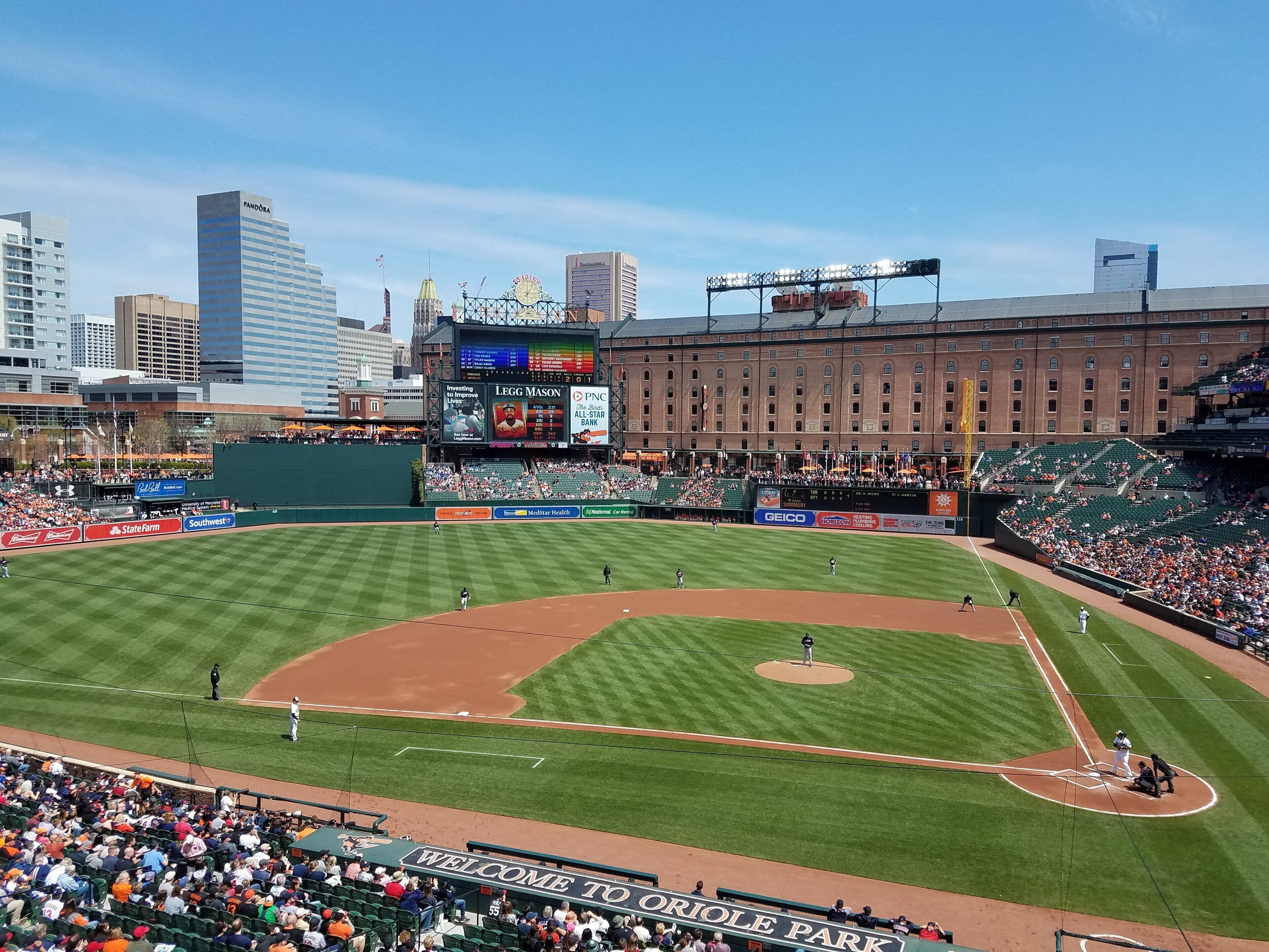 A baseball stadium with a large screen displaying game information, a well-maintained field, and a crowd of spectators.