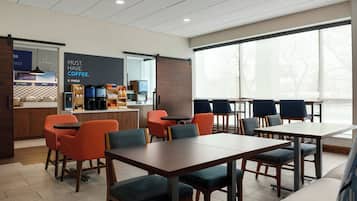 A modern cafe with tables and chairs, a coffee station, and large windows.