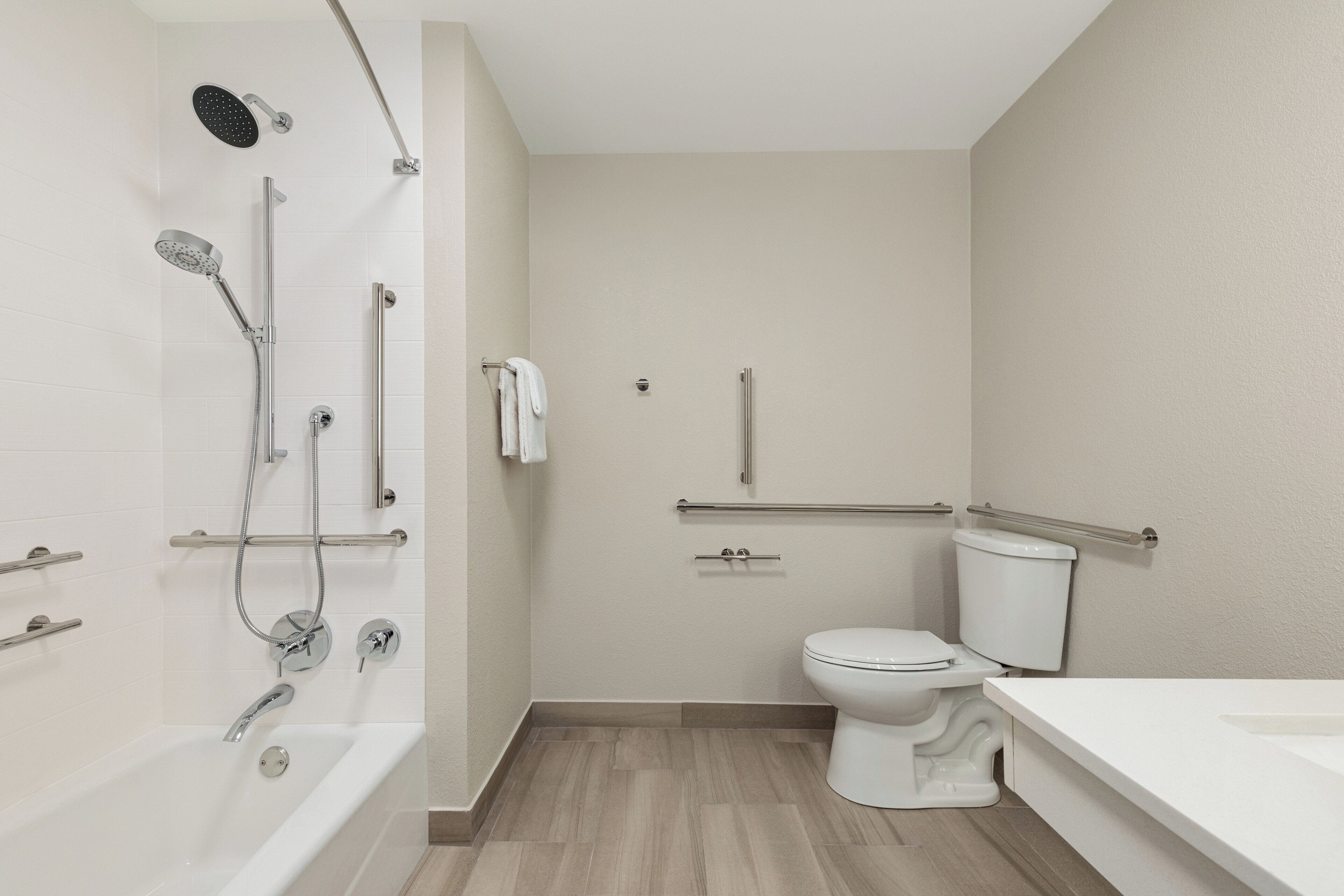 Ein modernes Badezimmer mit Badewanne, Dusche, Toilette und einer Haltestange zur Barrierefreiheit.