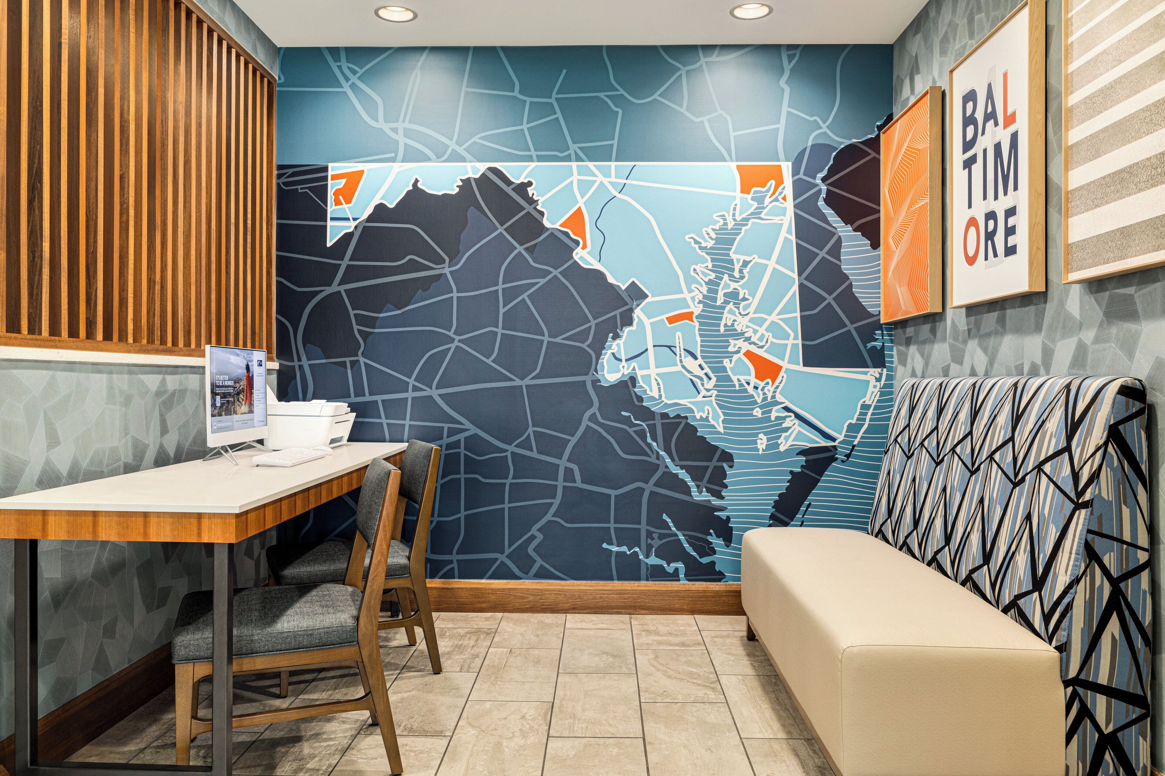 Un interior moderno con un mural de mapa, un separador de madera, un escritorio con computadora y un sofá estampado.