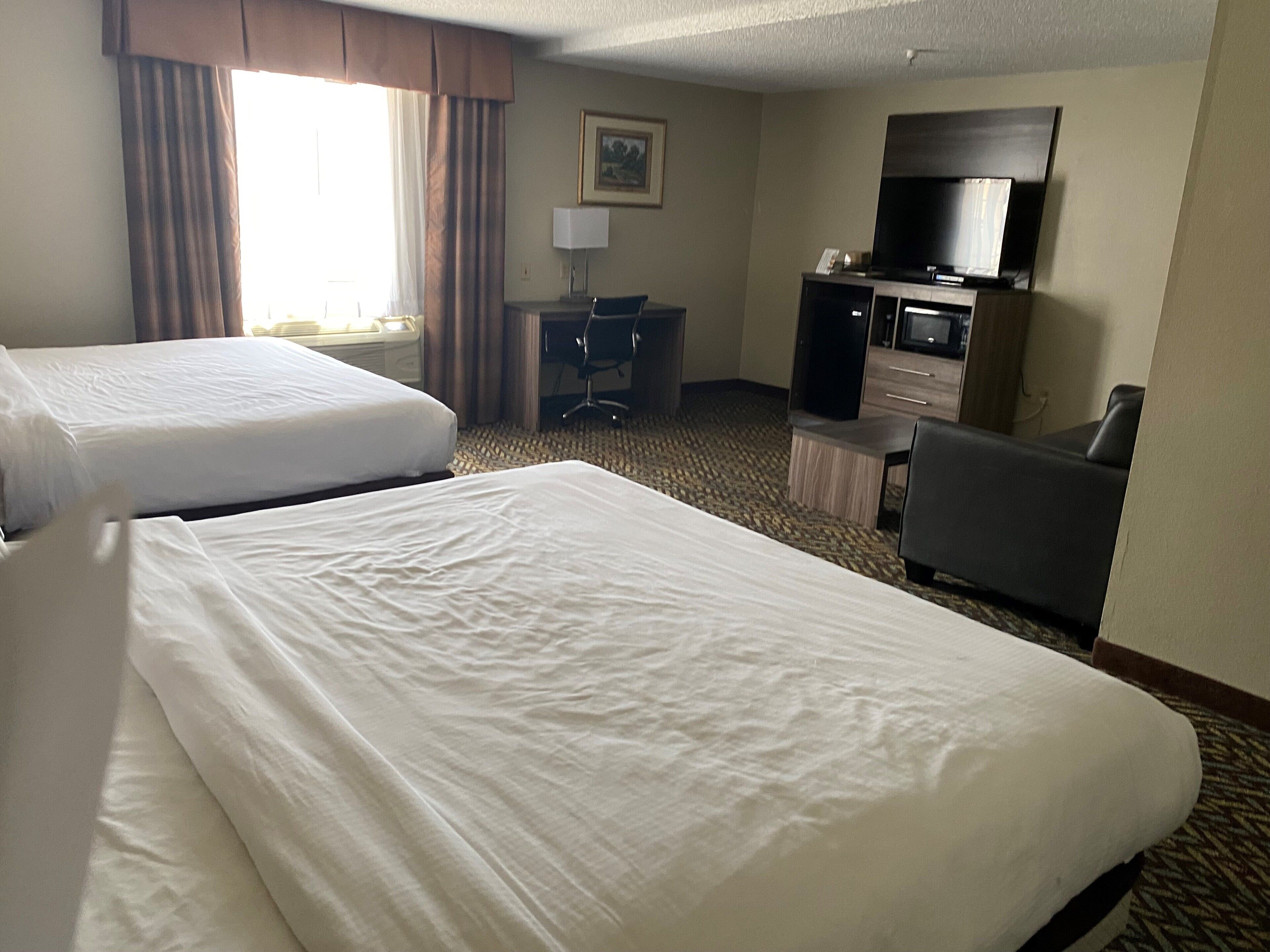 A hotel room with two beds, a desk, a chair, a television, and a carpeted floor.