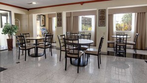 A hotel dining area with multiple round tables and chairs, a potted plant, and framed artwork on the walls. - Baymont by Wyndham Oklahoma City Airport (Oklahoma City)