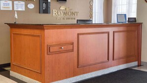 A reception desk at Baymont Inn & Suites with framed certificates, a welcome sign, and a television above it. - Baymont by Wyndham Oklahoma City Airport (Oklahoma City)
