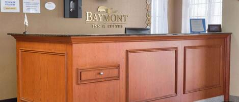 A reception desk at Baymont Inn & Suites with framed certificates, a welcome sign, and a television above it.