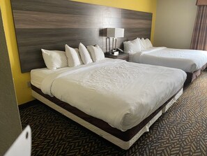 A hotel room with two beds, a wooden headboard, a bedside table with a lamp, and a patterned carpet.