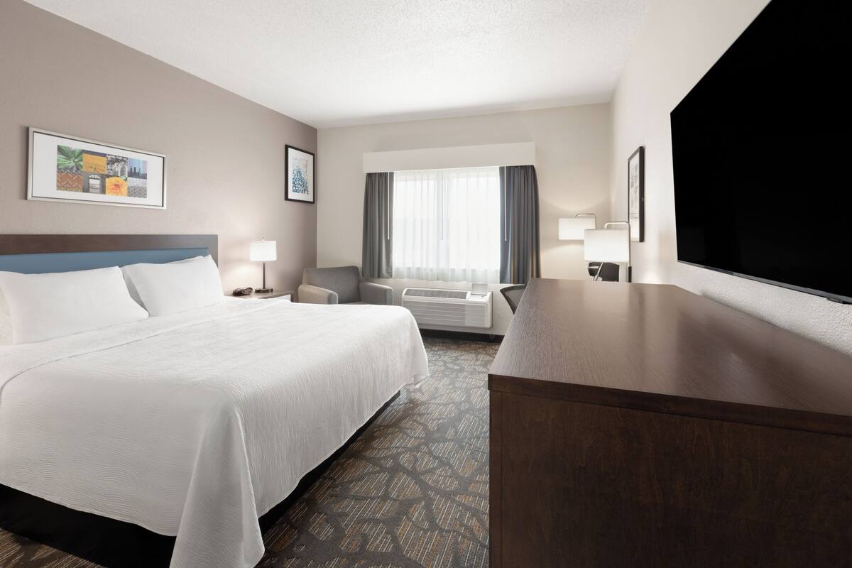 A hotel room with a large bed, a desk, a chair, a TV, and a window with curtains.