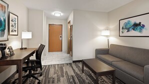 A hotel room with a desk, chair, sofa, and a patterned carpet. - Wingate by Wyndham Marion (Marion)