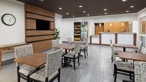 A modern restaurant with wooden tables and patterned chairs, a clock on the wall, and a Corner Market refrigerator. - Wingate by Wyndham Marion (Marion)
