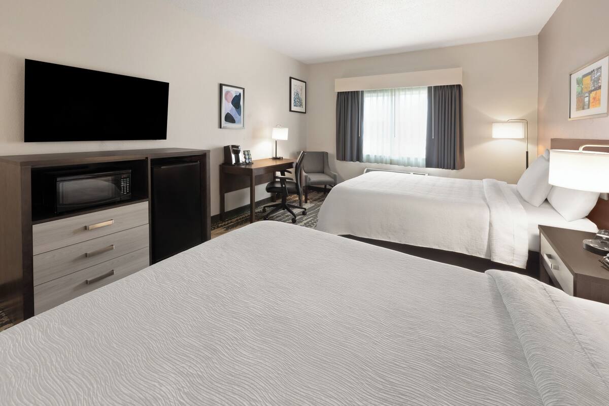A hotel room with two beds, a desk with a chair, a TV, a microwave, and a small refrigerator.