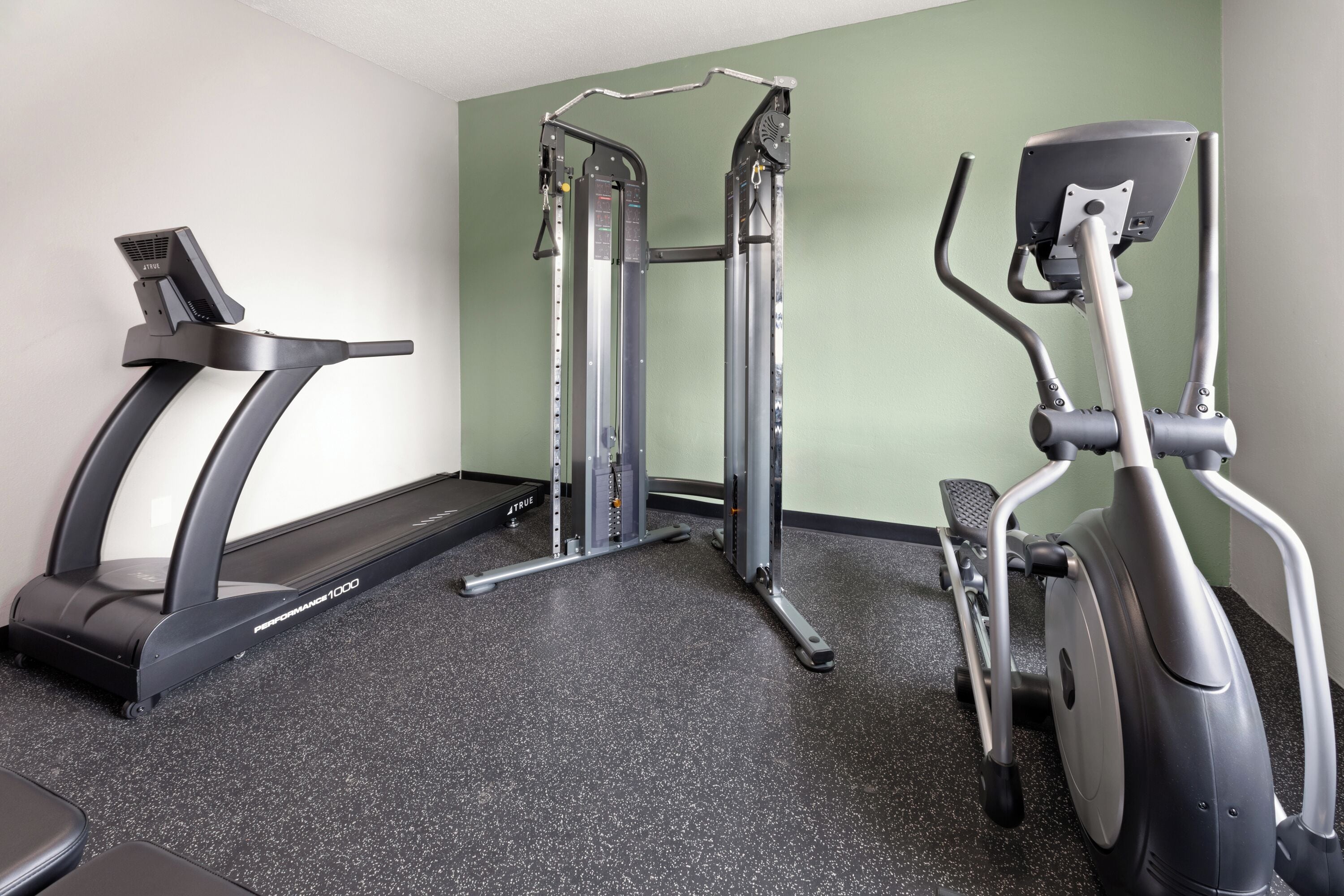 A gym with a treadmill, elliptical, and weight machine.