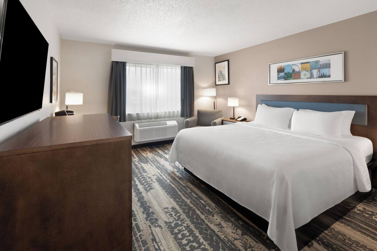 A hotel room with a large bed, a desk, a chair, a TV, and a window with curtains.