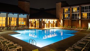 A swimming pool with lounge chairs and tables, surrounded by a building with large windows and brick walls. - Lincolnshire Marriott Resort (Lincolnshire)