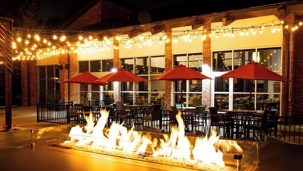An outdoor dining area with a fire feature, tables, chairs, and red umbrellas. - Lincolnshire Marriott Resort (Lincolnshire)