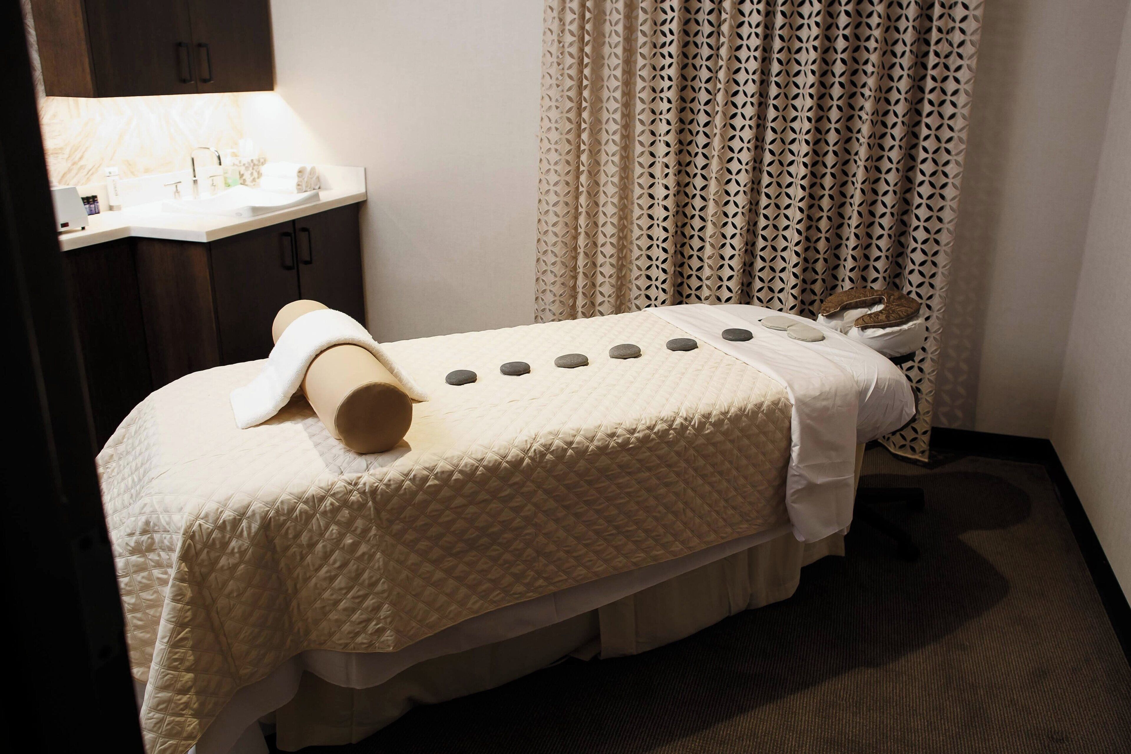 A neatly made bed with a quilted cover, a towel, and a pair of slippers.