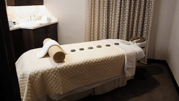 A neatly made bed with a quilted cover, a towel, and a pair of slippers.