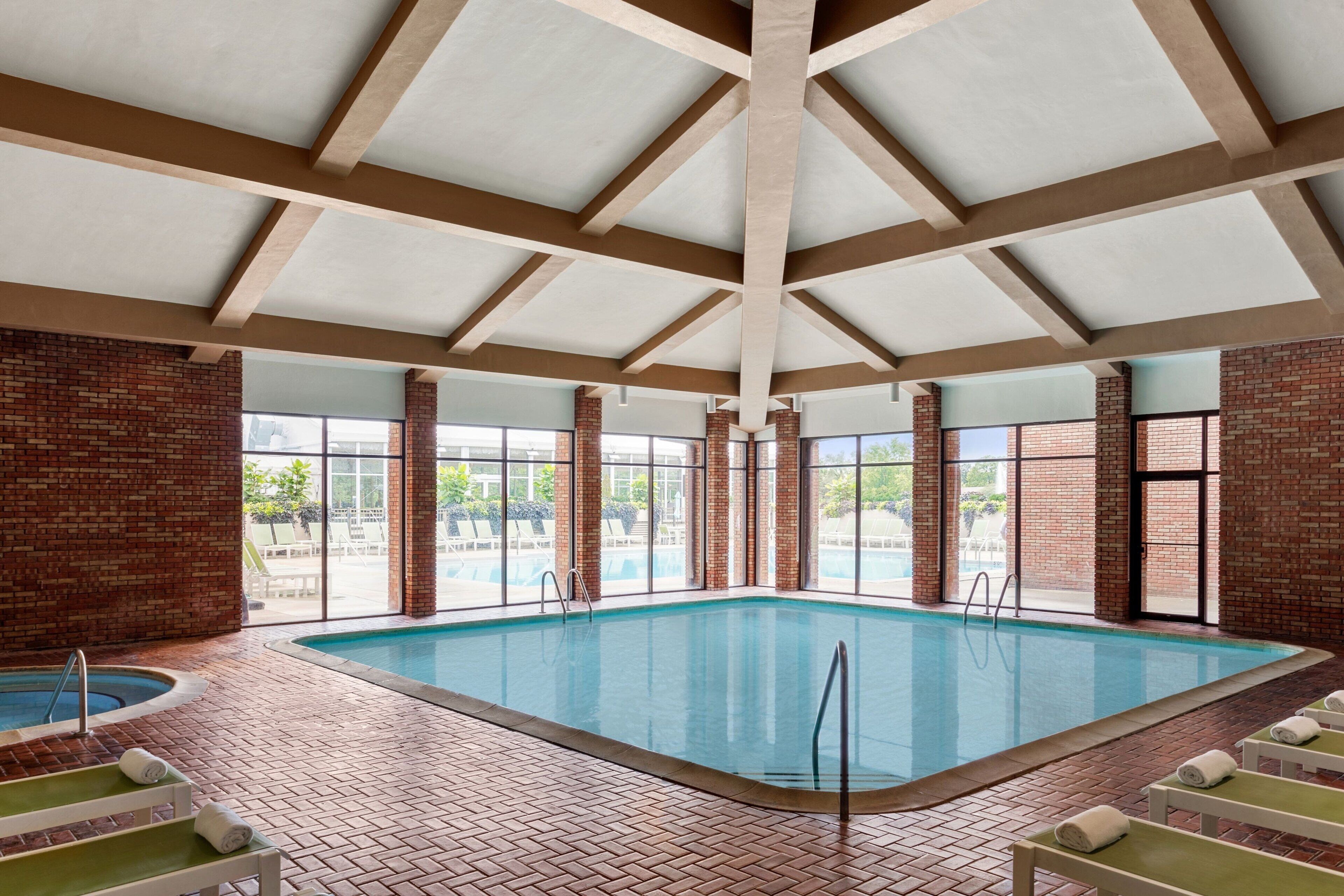 Una piscina interior con suelo de ladrillo, ventanas amplias y un techo alto con vigas de madera.