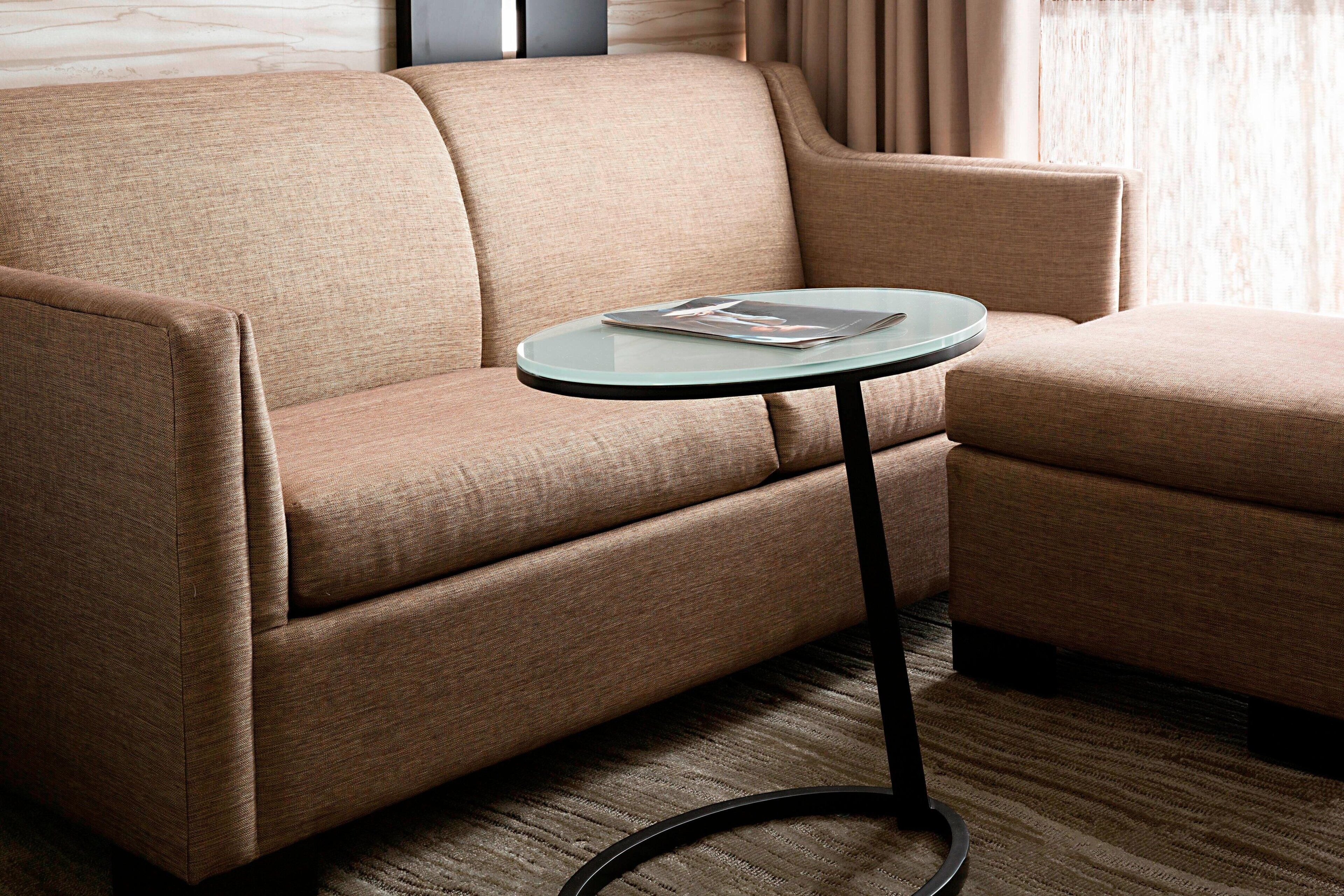 En beige sofa med et sofabord med glasplade i et moderne rum med et mønstret tæppe.