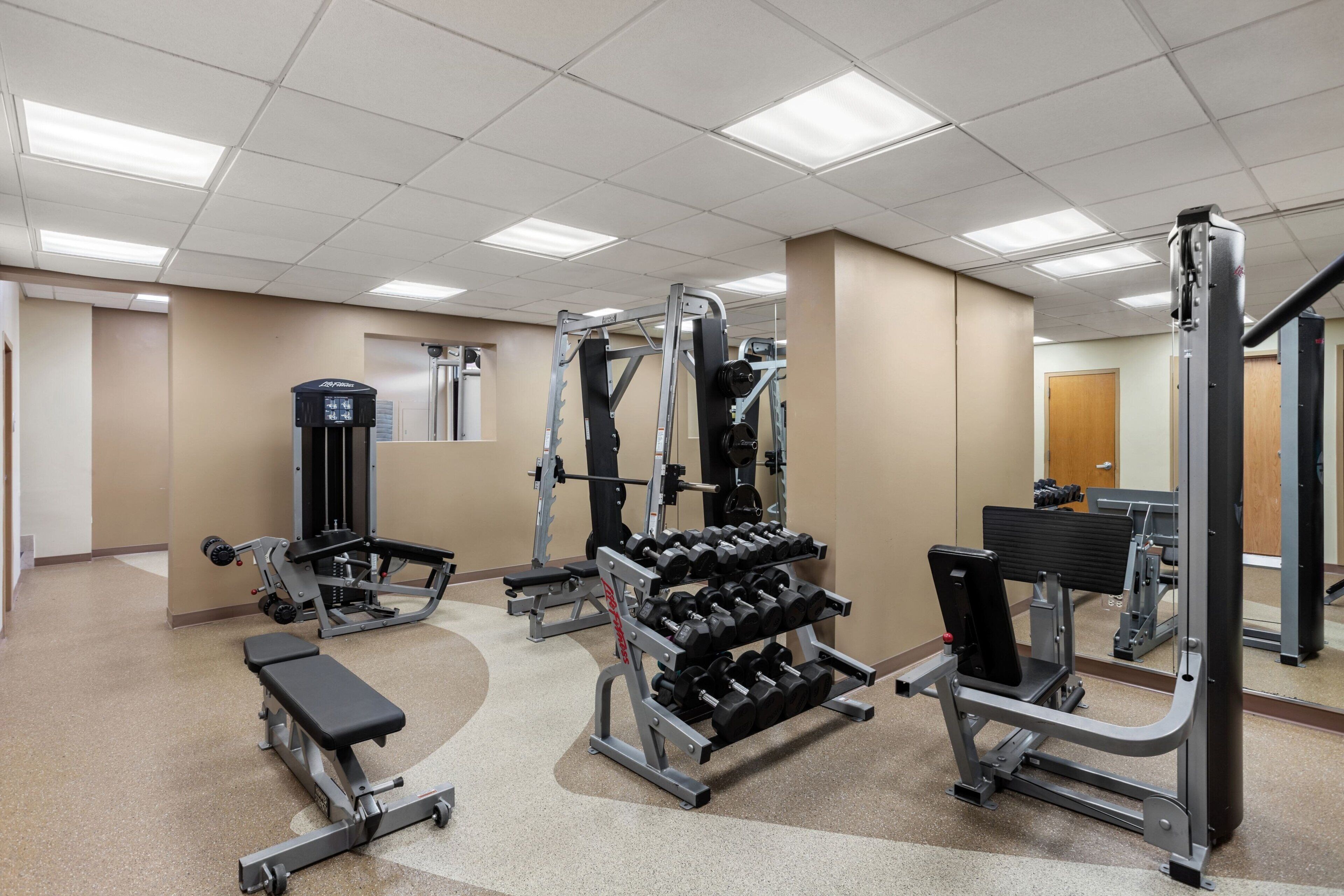 A gym with various exercise equipment including dumbbells, benches, and weight machines.