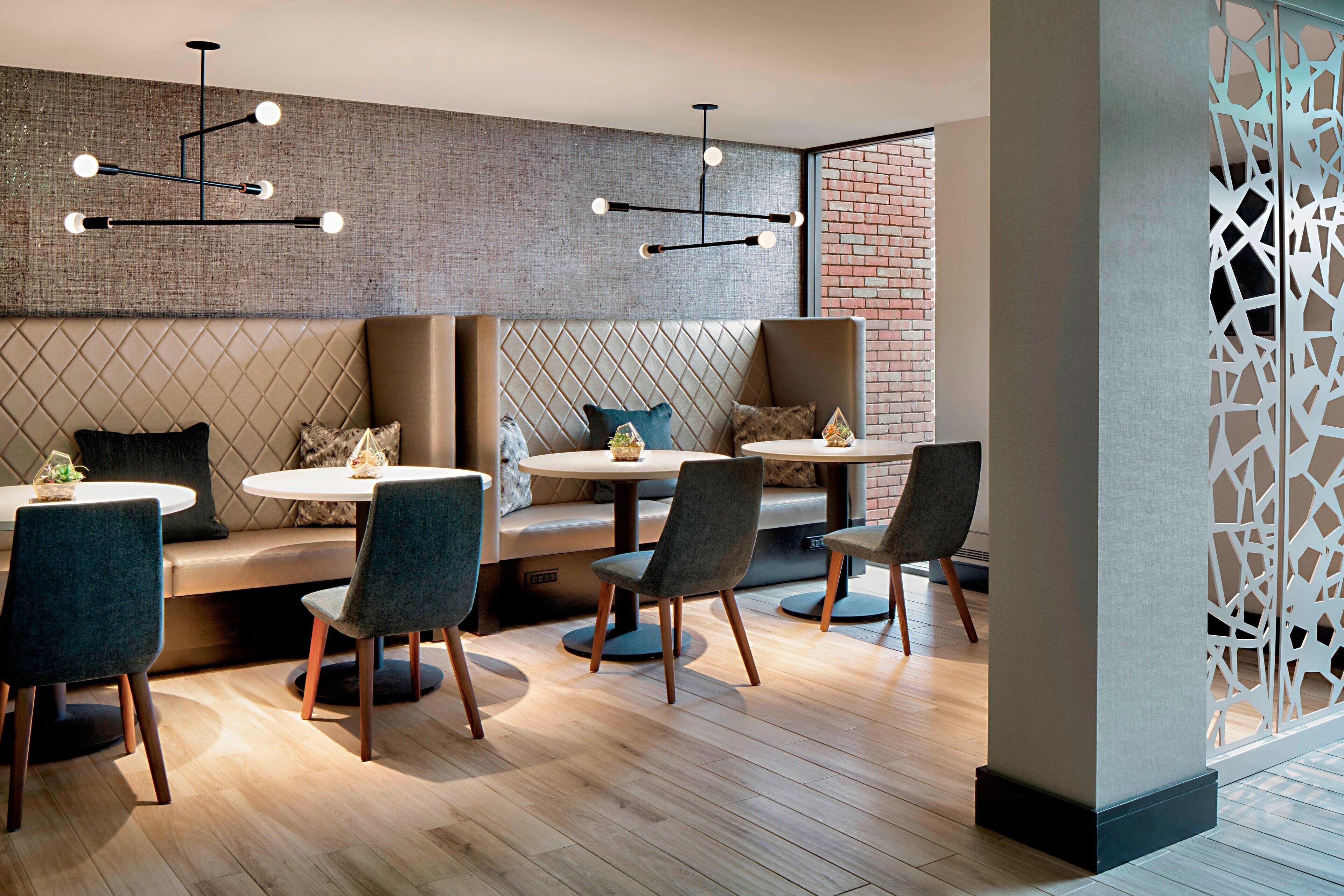 A modern dining area with round tables and chairs, a brick wall, and decorative lighting.