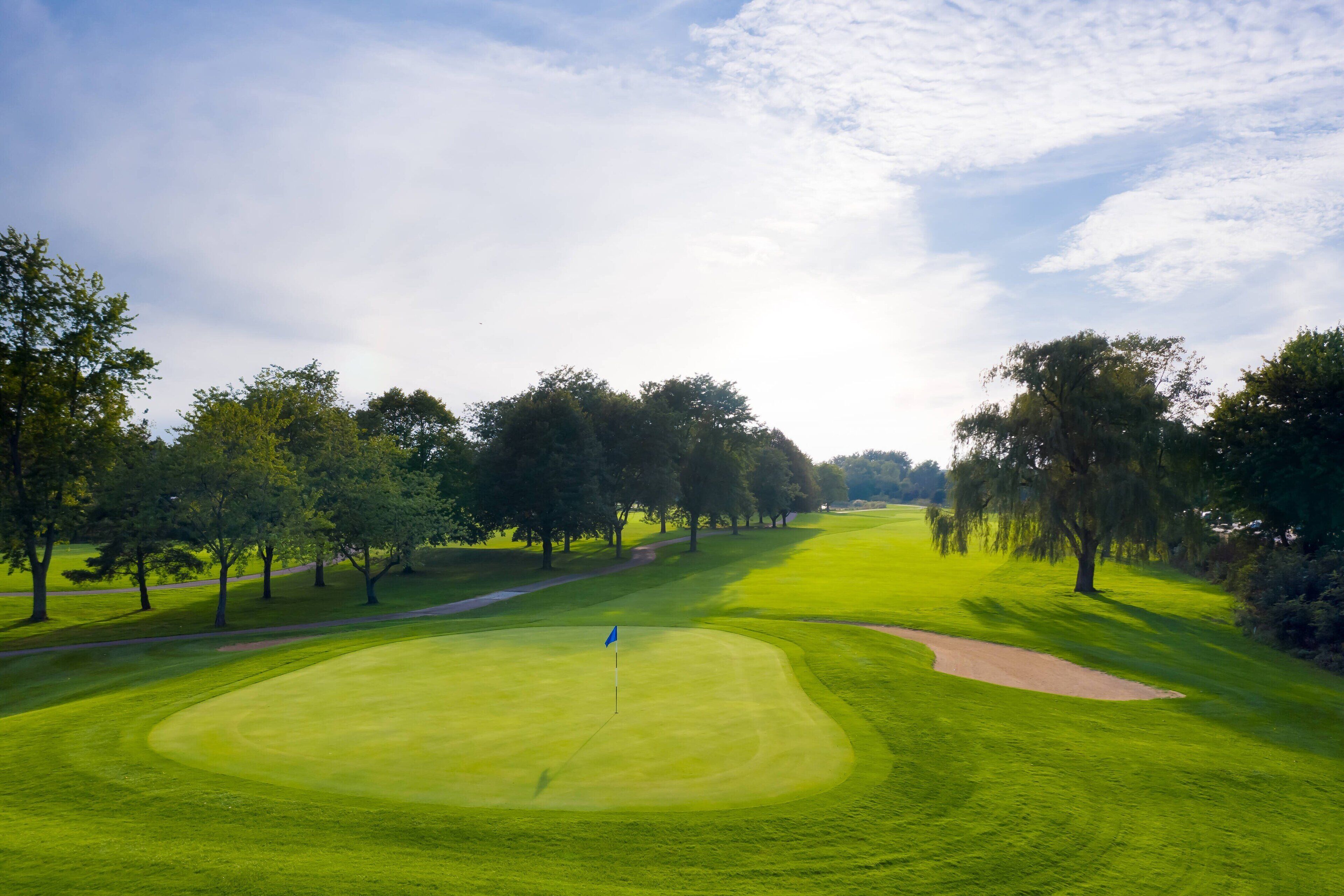 A golf course with a flag on the green, surrounded by trees and a clear sky.