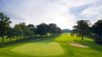 A golf course with a flag on the green, surrounded by trees and a clear sky.