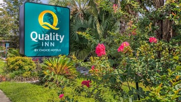 A sign for Quality Inn by Choice Hotels surrounded by lush greenery and flowering plants.