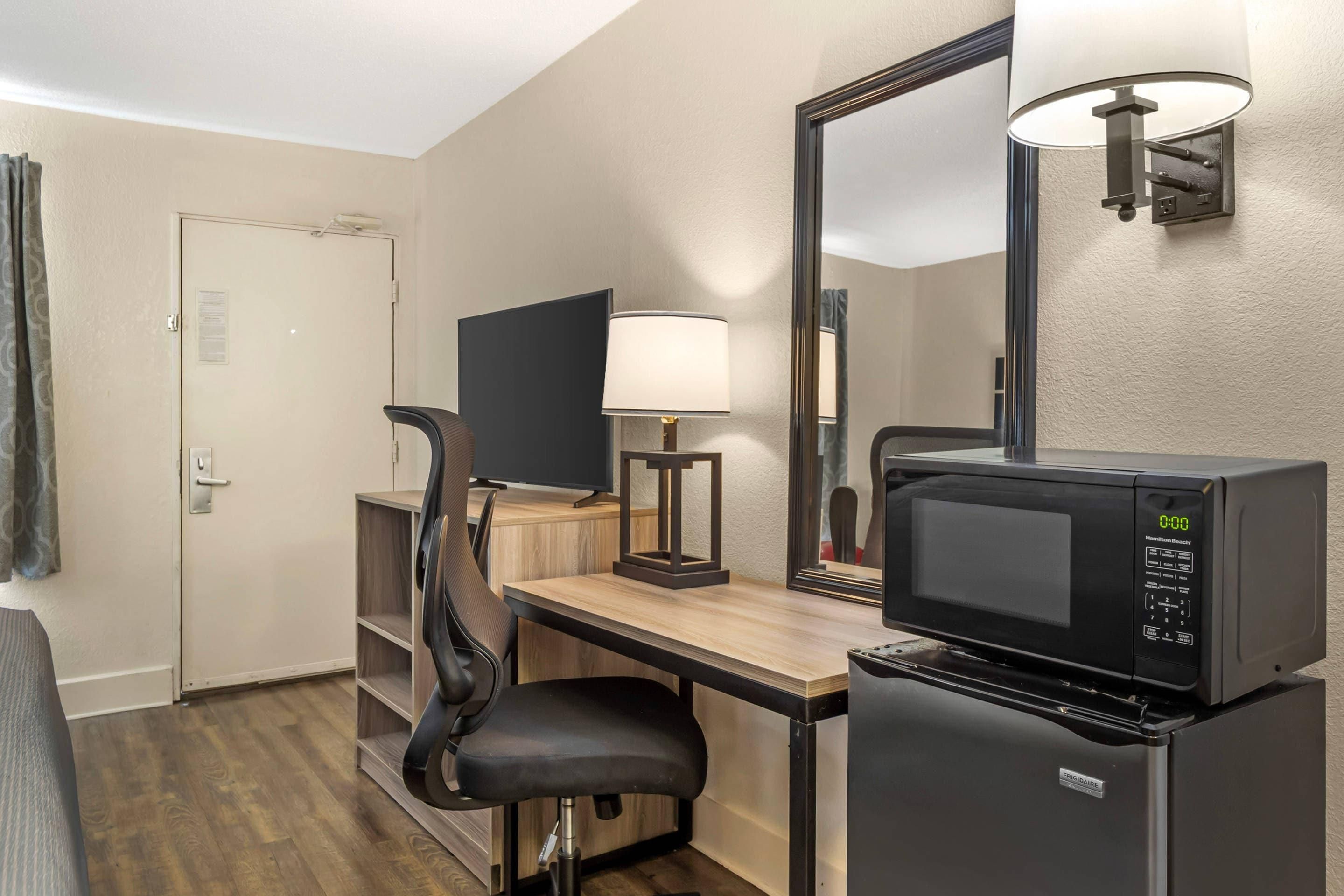 Habitación de hotel con escritorio, silla, microondas y un espejo grande.