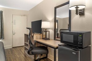 Ein Hotelzimmer mit Schreibtisch, Stuhl, Mikrowelle und einem großen Spiegel.