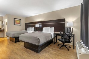 A hotel room with two beds, a desk, a chair, a lamp, and an air conditioning unit. - Quality Inn Goose Creek - Charleston (Goose Creek)