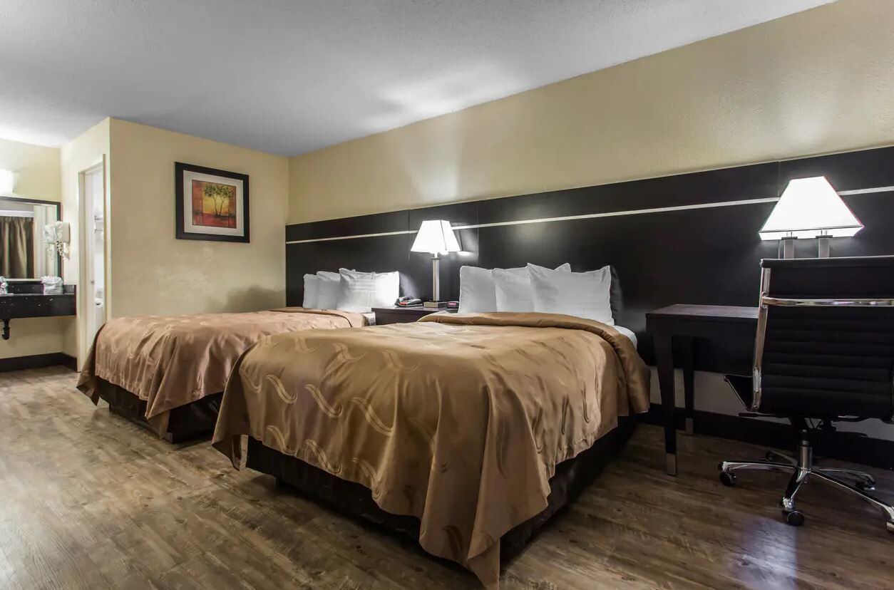 A hotel room with two beds, a desk, and a chair.