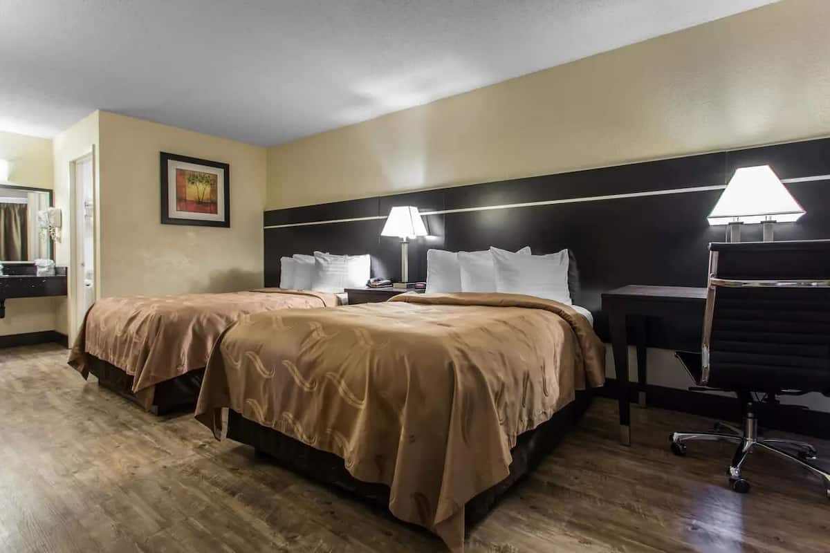 A hotel room with two beds, a desk, and a chair.