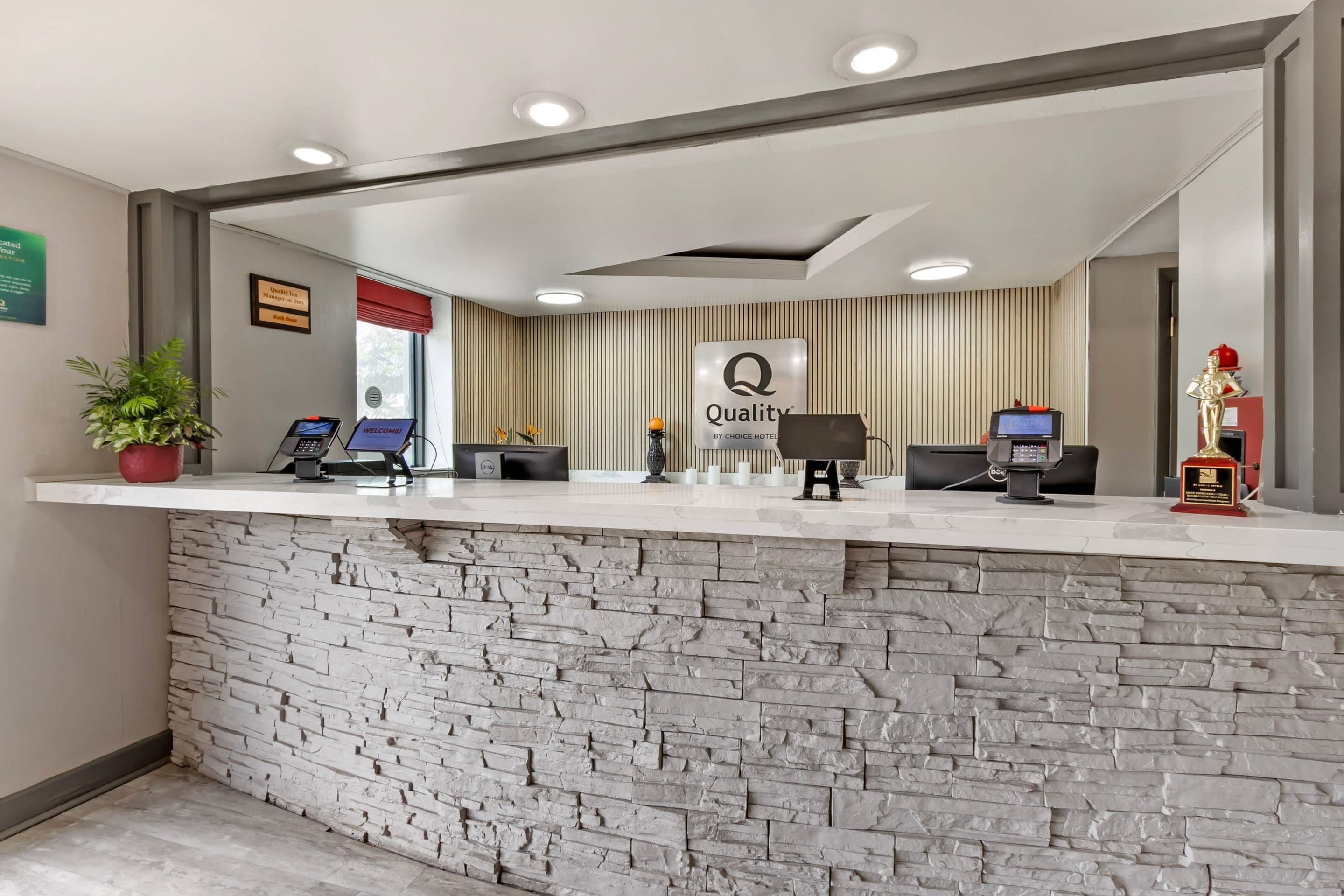 Un mostrador de recepción de hotel con fachada de piedra, un cartel de 'Quality by Choice Hotel' y dos quioscos de recepción.