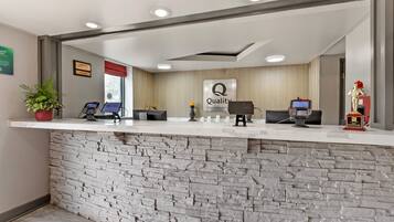 Un mostrador de recepción de hotel con fachada de piedra, un cartel de 'Quality by Choice Hotel' y dos quioscos de recepción.