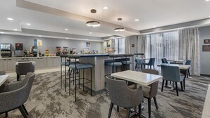 Un hall d’hôtel moderne doté d’un bar, de différents espaces de détente et d’une grande fenêtre agrémentée de rideaux.