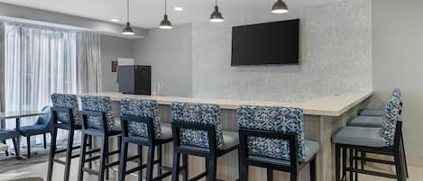 A modern kitchen with a bar area, bar stools, a flat-screen TV, and pendant lighting.