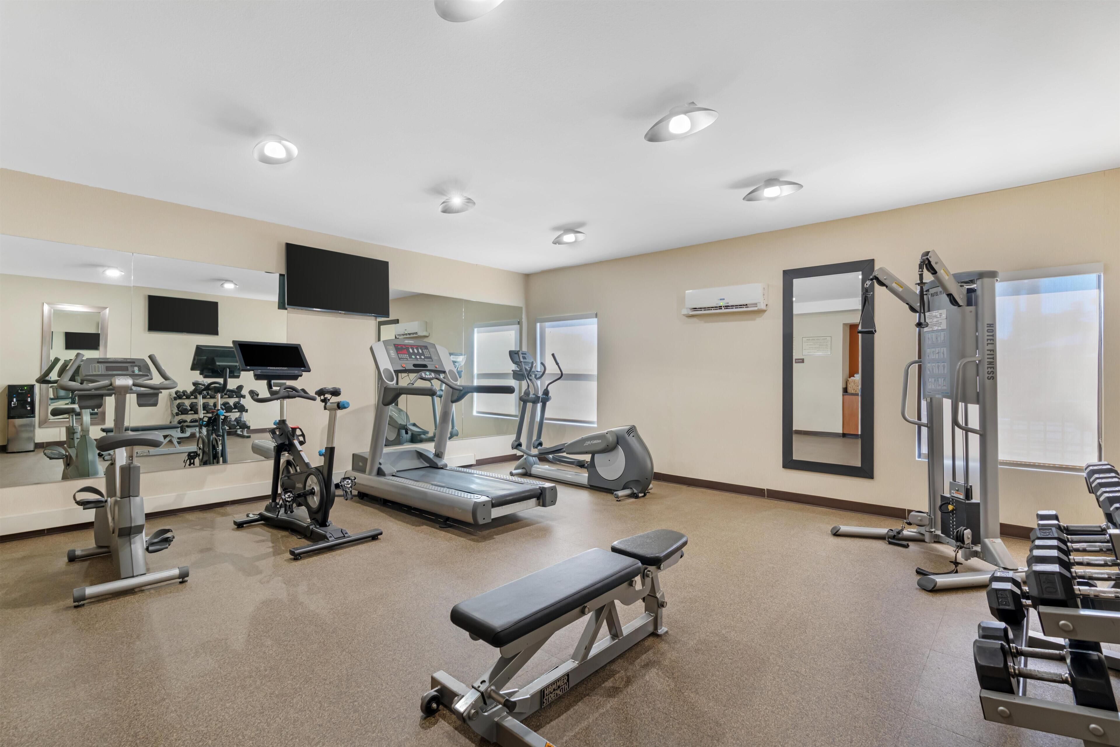 Ein Fitnessraum mit Laufbändern, Crosstrainern, einer Bank und Kurzhanteln.