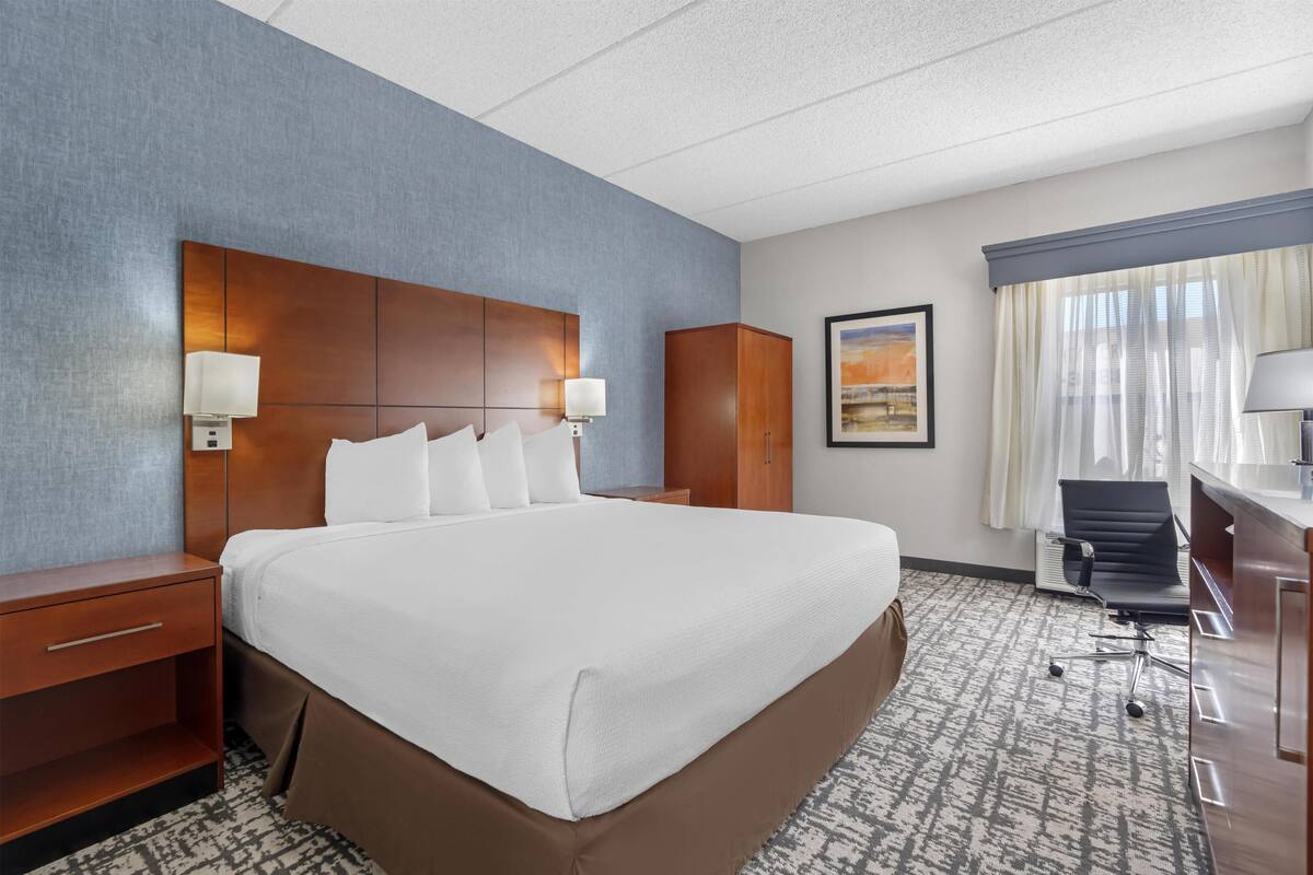 Une chambre d’hôtel avec un grand lit, deux tables de chevet, un bureau avec une chaise et une fenêtre avec des rideaux.