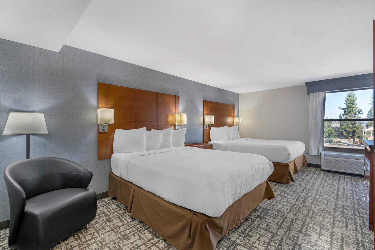 Une chambre d’hôtel avec deux lits, une chaise, une lampe et une grande fenêtre.