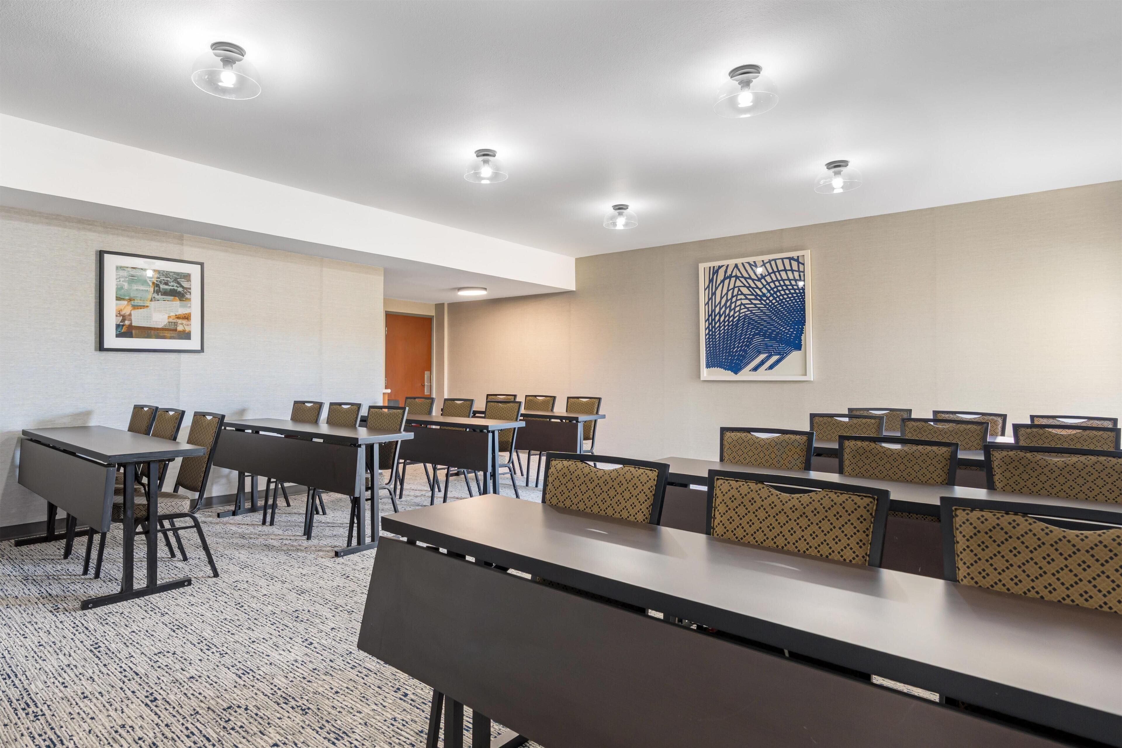 A conference room with tables and chairs, recessed ceiling lights, a framed picture, and a large abstract painting on the wall.