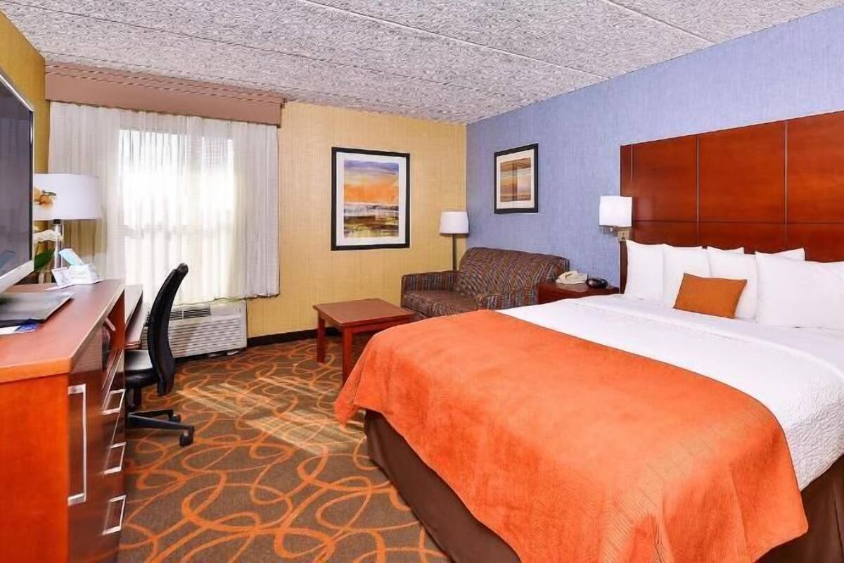 Une chambre d’hôtel avec un lit, un bureau, une chaise et deux tableaux accrochés au mur.