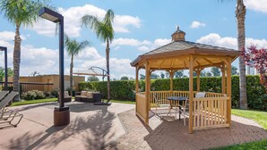 Un kiosque avec une table et des chaises, entouré de palmiers et bordé d’une terrasse en briques.